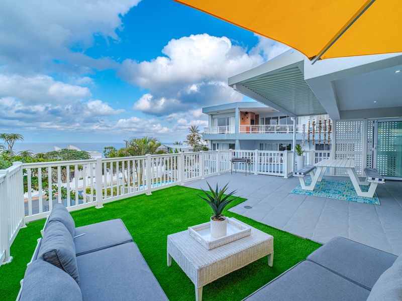 Spacious elevated balcony featuring a combination of tiled flooring and artificial turf, protected by a retractable awning and white balustrade with ocean views.