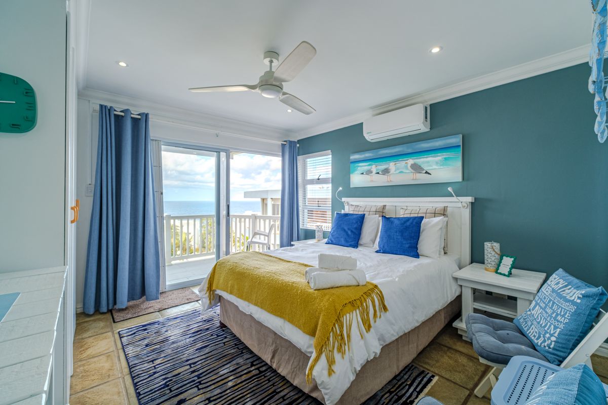 A well-maintained bedroom featuring a ceiling fan, split-system air conditioning, and direct access to a private balcony with ocean views.