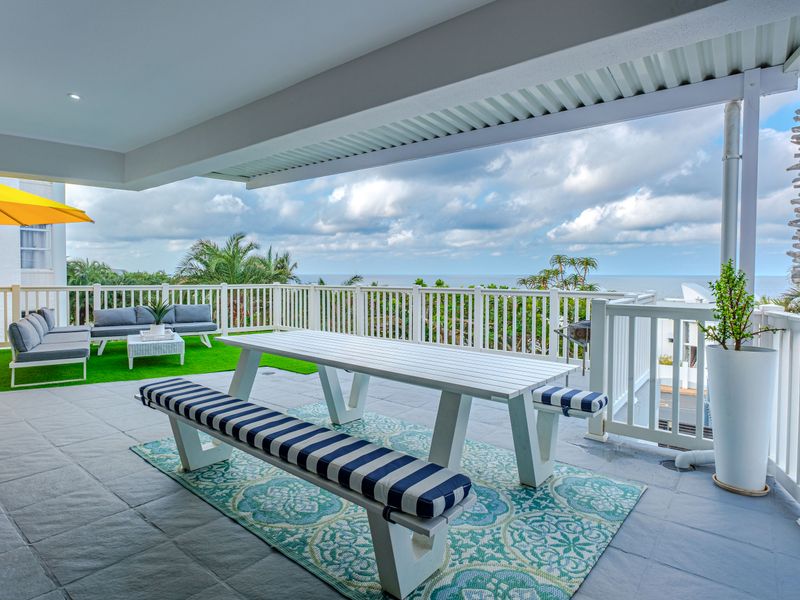 Spacious covered balcony featuring tiled flooring, white railings, and panoramic ocean views, perfect for outdoor dining and relaxation.