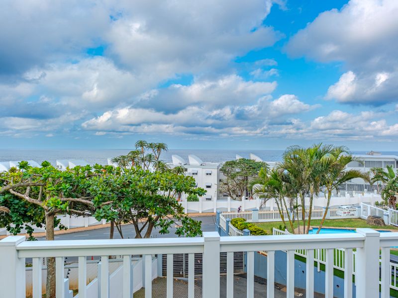 Elevated coastal view overlooking a residential complex, swimming pool, and the ocean horizon from a balcony.