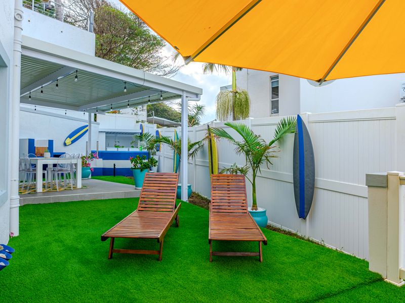 A well-maintained outdoor patio area featuring a covered seating space, synthetic lawn, and a built-in bar, perfect for relaxed outdoor entertaining.