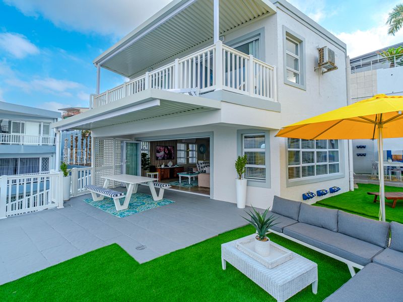 Rear view of a two-story house featuring a covered patio, upper balcony, and a landscaped outdoor area with artificial turf.