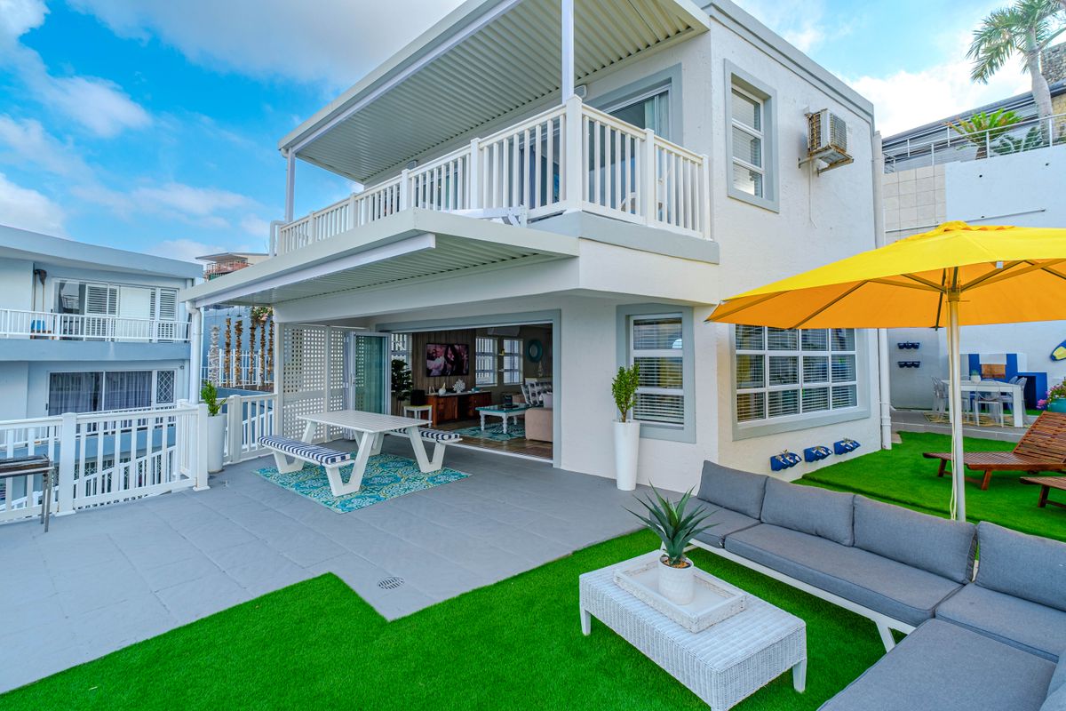 Rear view of a two-story house featuring a covered patio, upper balcony, and a landscaped outdoor area with artificial turf.