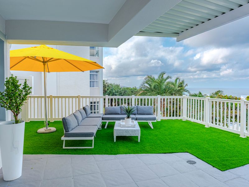 A spacious covered balcony featuring tiled flooring, artificial turf, and a protective railing, offering an outdoor living space with scenic views.