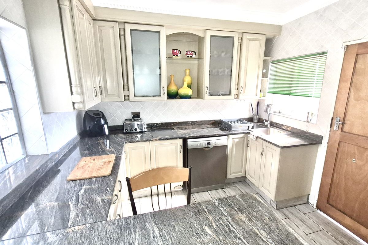 A functional kitchen featuring granite countertops, ample built-in cabinetry, an integrated dishwasher, and a stainless steel sink with a tiled backsplash.