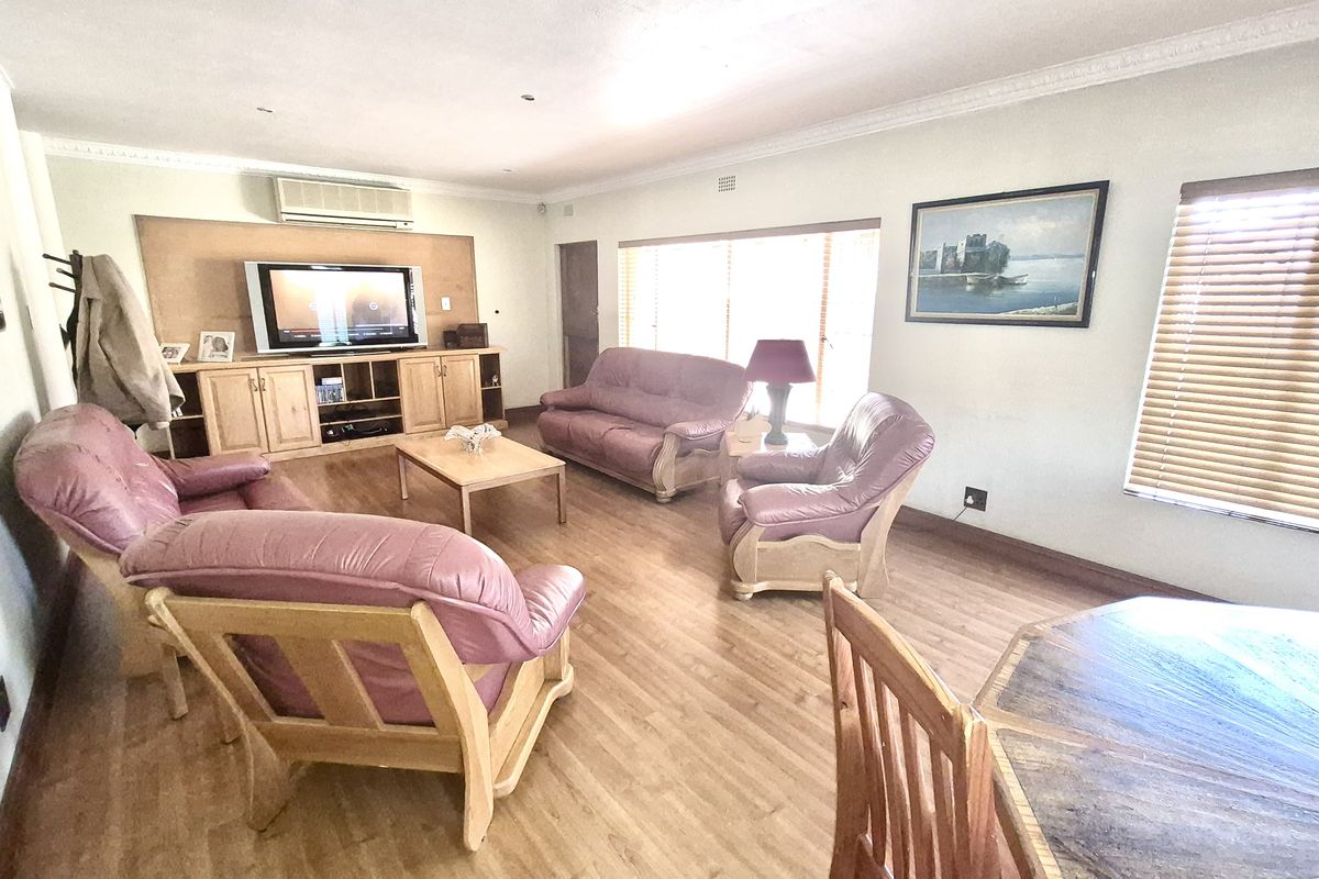 Spacious living room featuring laminate flooring, built-in wooden cabinetry, and a wall-mounted air conditioning unit, offering a comfortable and functional living space.