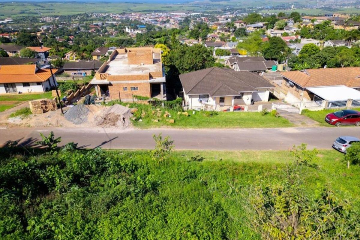 Aerial view of a vacant residential plot situated in an established neighborhood with surrounding housing and distant coastal views.