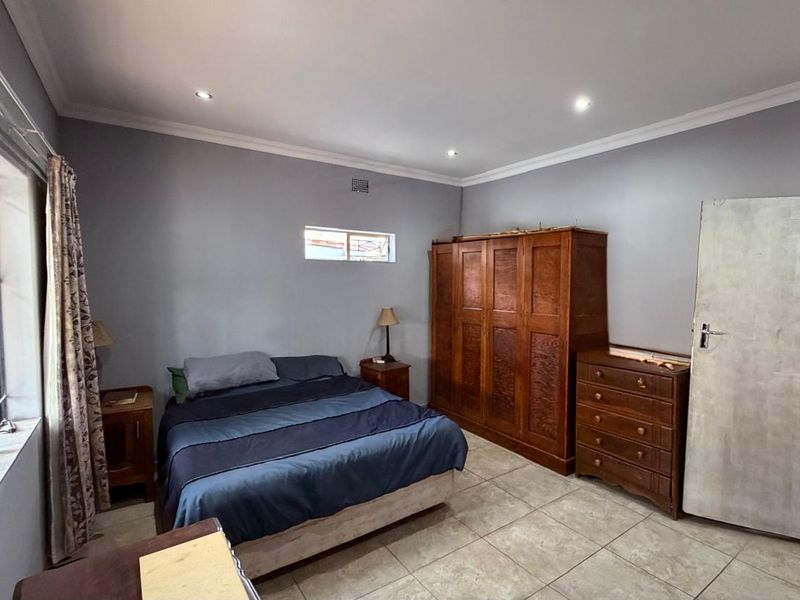 A spacious bedroom featuring tiled flooring, recessed downlighting, and neutral wall tones, offering a functional layout with built-in storage potential.