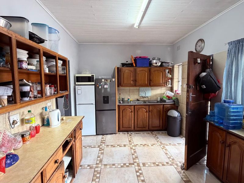 A functional kitchen featuring wooden cabinetry, laminate countertops, a double bowl sink, and tiled flooring, offering potential for modernization.