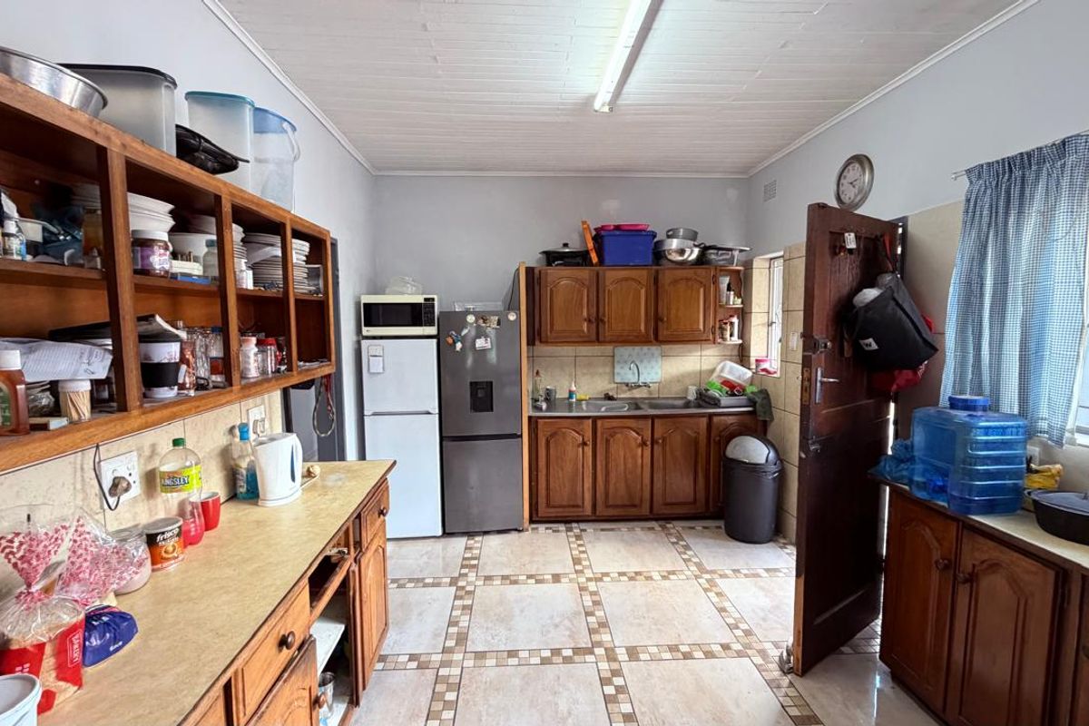 A functional kitchen featuring wooden cabinetry, laminate countertops, a double bowl sink, and tiled flooring, offering potential for modernization.