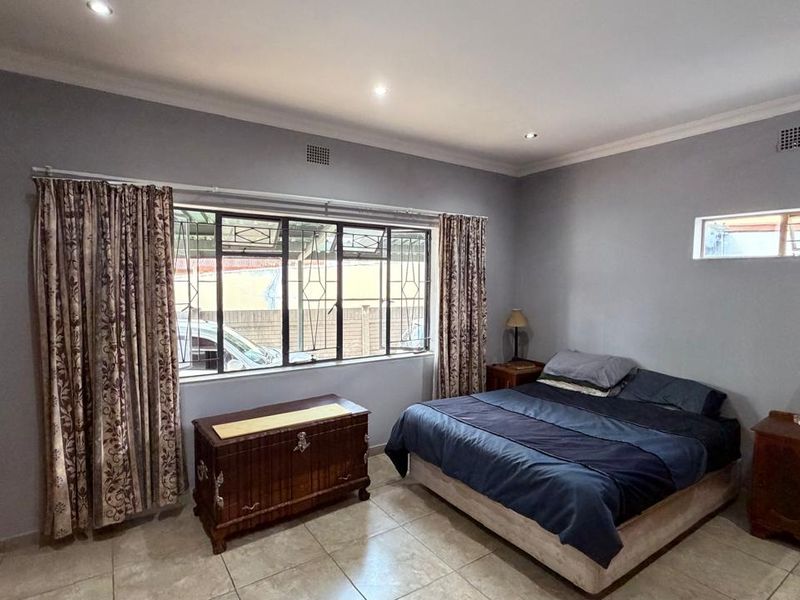 A spacious bedroom featuring tiled flooring, built-in cupboards, recessed downlighting, and security bars on the windows.