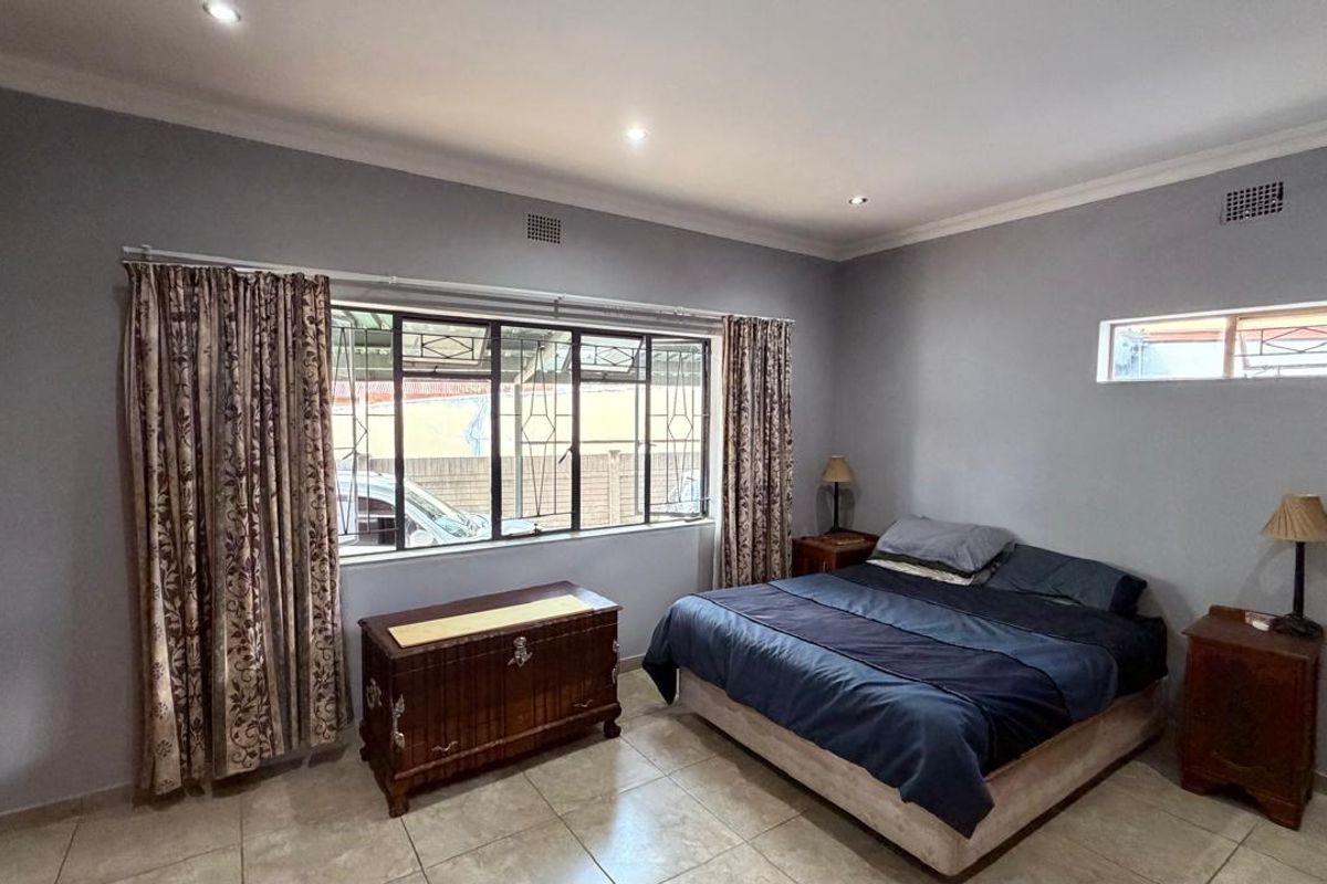 A spacious bedroom featuring tiled flooring, built-in cupboards, recessed downlighting, and security bars on the windows.