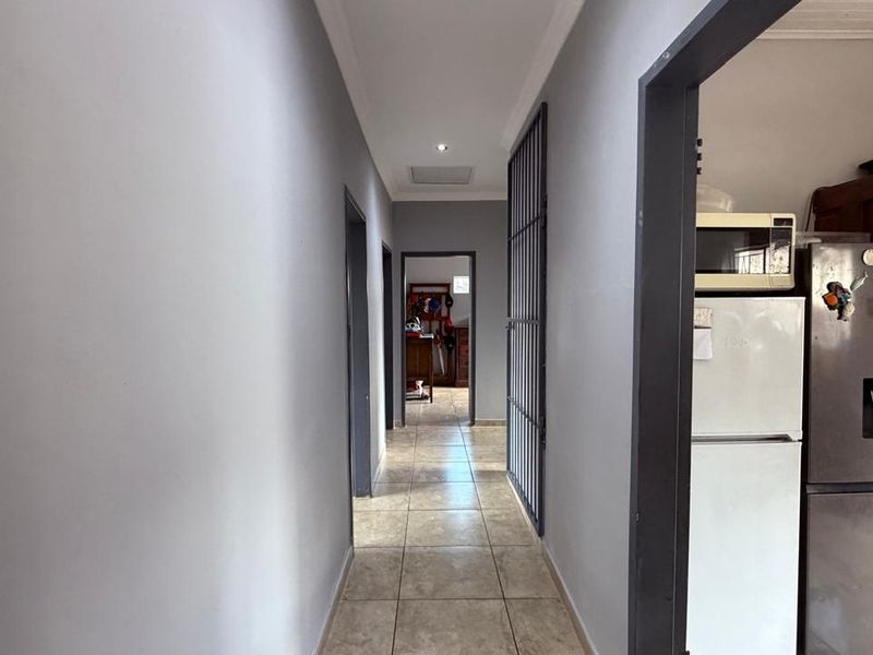 A neutral-toned hallway featuring tiled flooring, recessed lighting, and a security gate, providing access to adjacent rooms within the home.