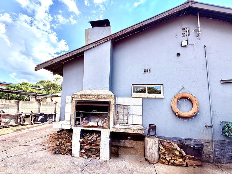 Rear exterior view featuring a built-in brick braai area, concrete paving, and a perimeter boundary wall.