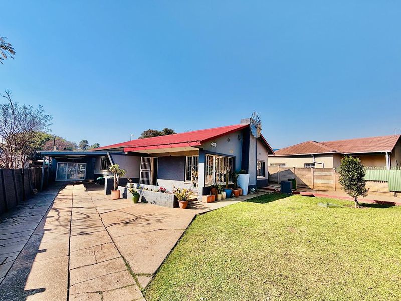 Front view of a single-story house featuring a red corrugated metal roof, concrete driveway, and a small front garden area.