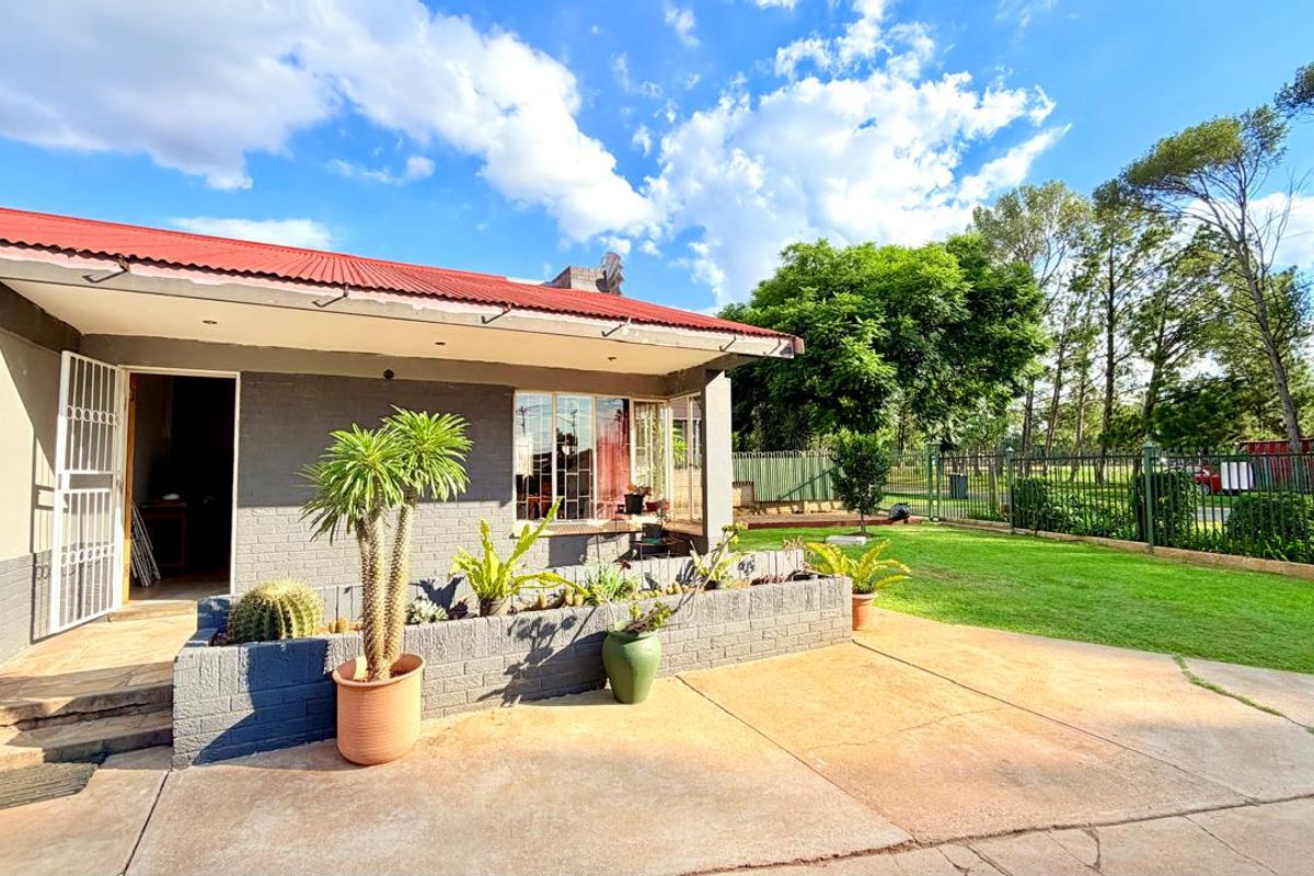 Rear exterior view of the house featuring a concrete patio, brick planter box, and a corrugated metal roof, set against a landscaped garden.