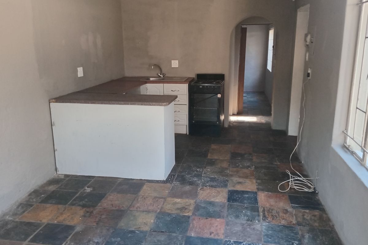 A basic, unfinished kitchen area featuring slate tile flooring, built-in cabinetry with a laminate countertop, and a freestanding stove.