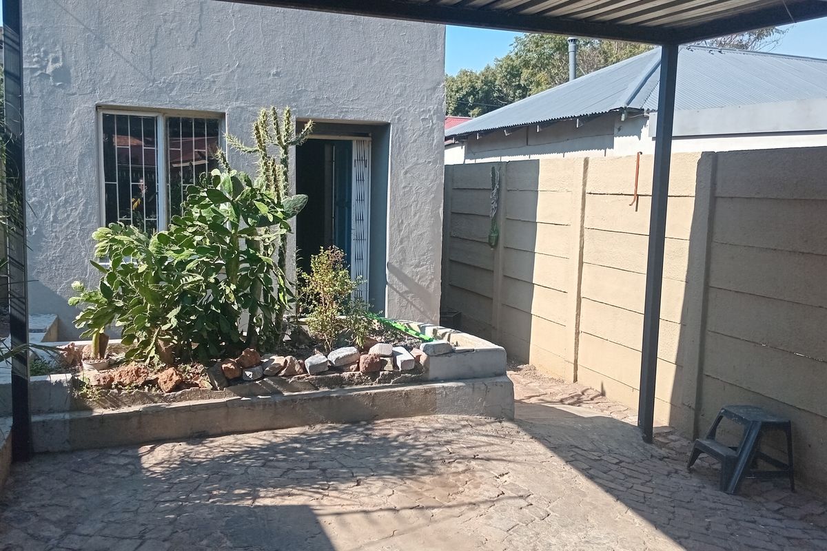 Rear exterior area featuring a covered patio, raised garden bed, and secure boundary walling, providing a functional outdoor space.
