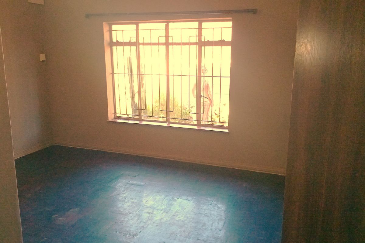 An empty bedroom featuring a window with security bars and a built-in cupboard, requiring some cosmetic updates to the flooring.