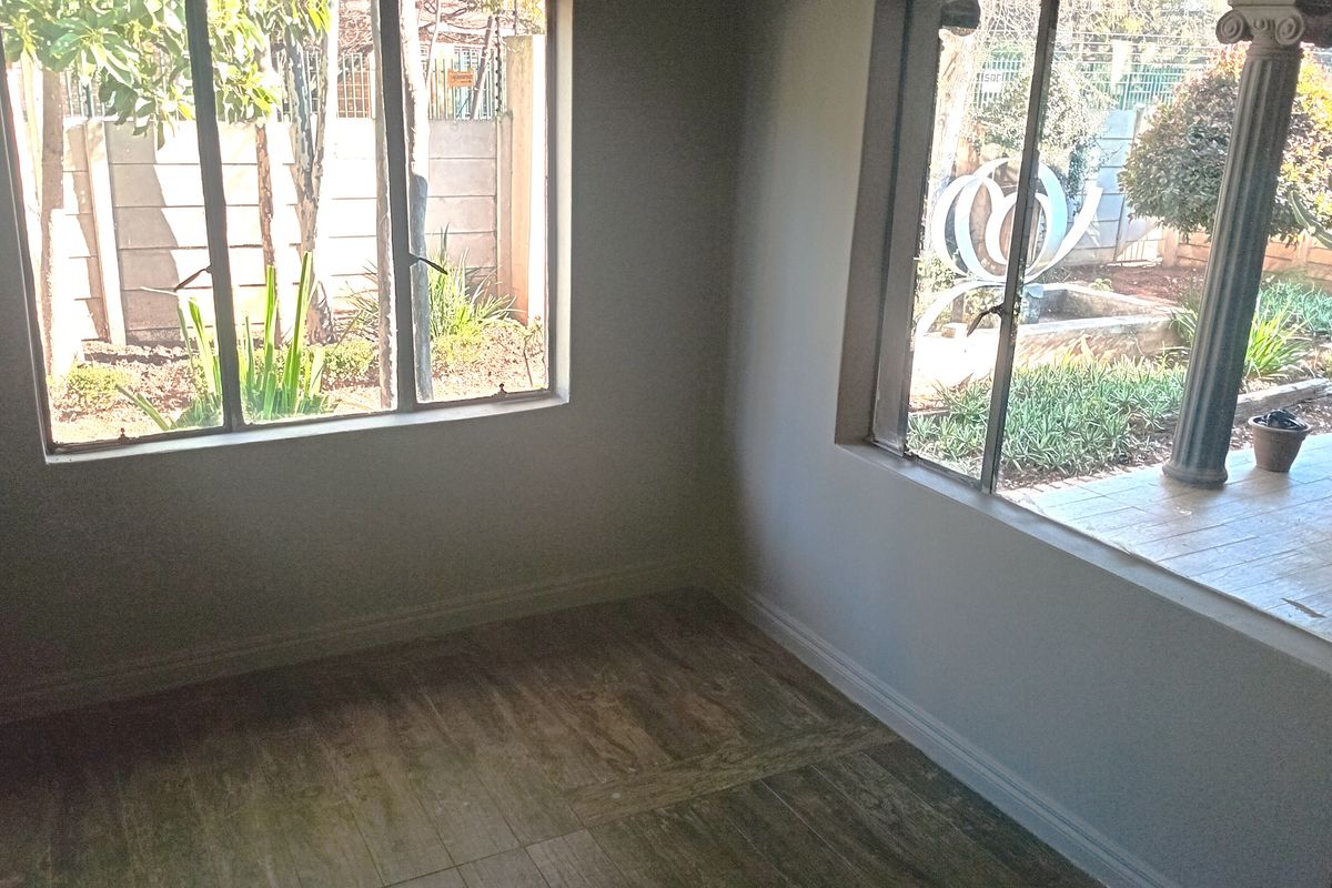 A bright, empty living area featuring wood-look tiled flooring and large windows overlooking the garden.