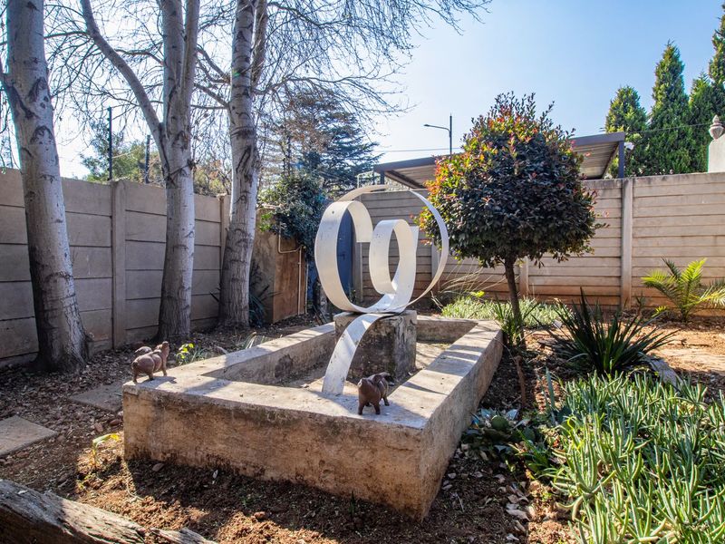A private garden area featuring a concrete boundary wall, a central water feature base, and established trees with a paved walkway.