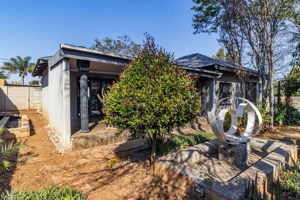 Rear view of the property featuring a covered patio, concrete columns, and a garden area with established trees and masonry boundary walls.