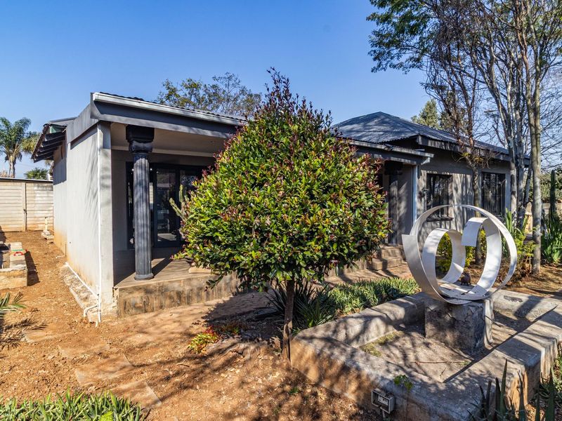 Rear view of the property featuring a covered patio, concrete columns, and a garden area with established trees and masonry boundary walls.