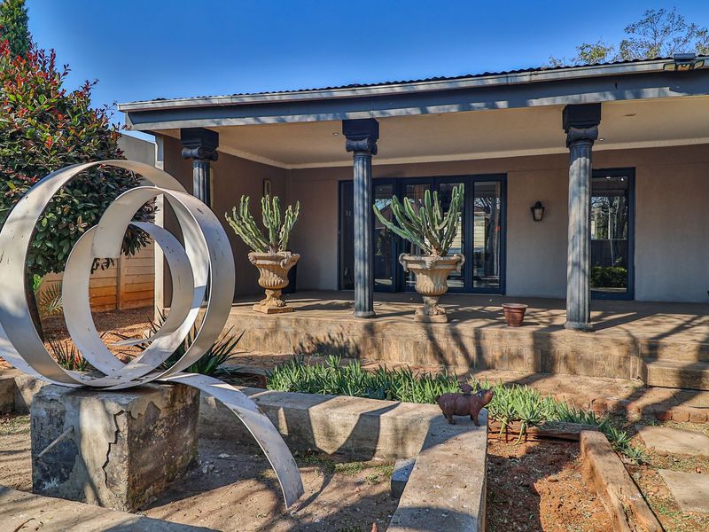 A covered outdoor patio area featuring decorative columns and tiled flooring, providing a shaded space overlooking the garden.