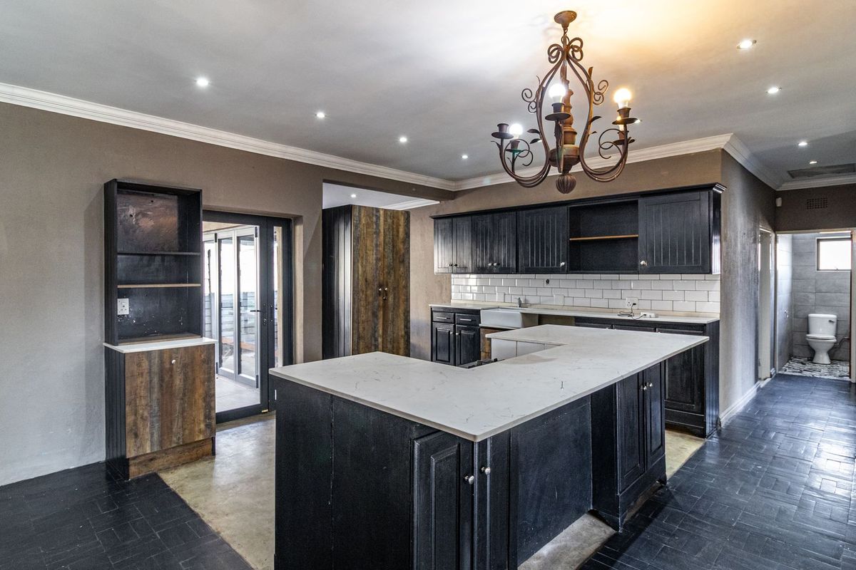 Spacious kitchen featuring dark cabinetry, a large u-shaped island, subway tile backsplash, and a farmhouse sink, complemented by a decorative chandelier.