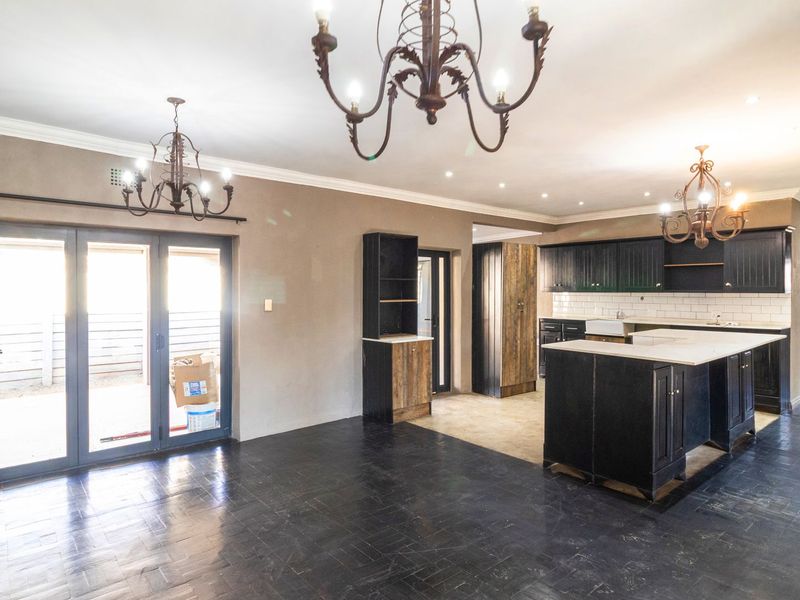 Spacious open-plan kitchen and living area featuring dark cabinetry, a central island, farmhouse sink, and folding glass doors leading to the exterior.