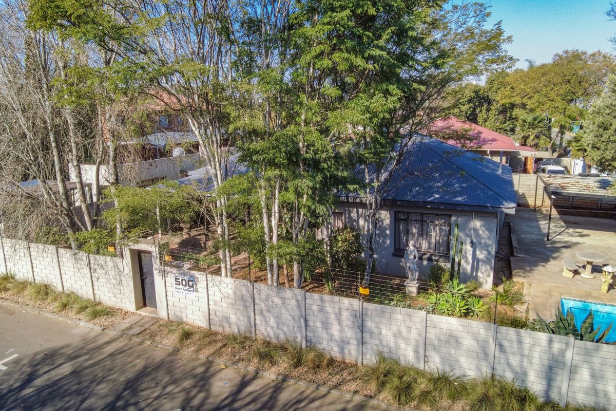 Aerial view of a residential property featuring a main house with a metal roof, a swimming pool, and a concrete block boundary wall.