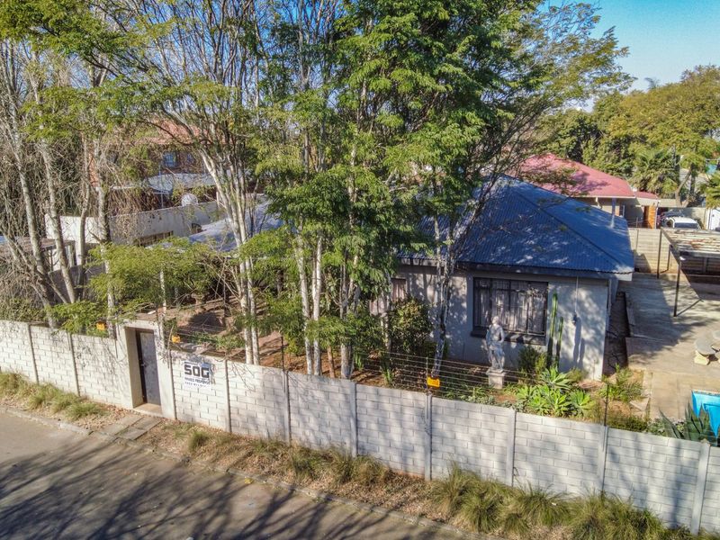 Aerial view of a residential property featuring a main house with a metal roof, a swimming pool, and a concrete block boundary wall.