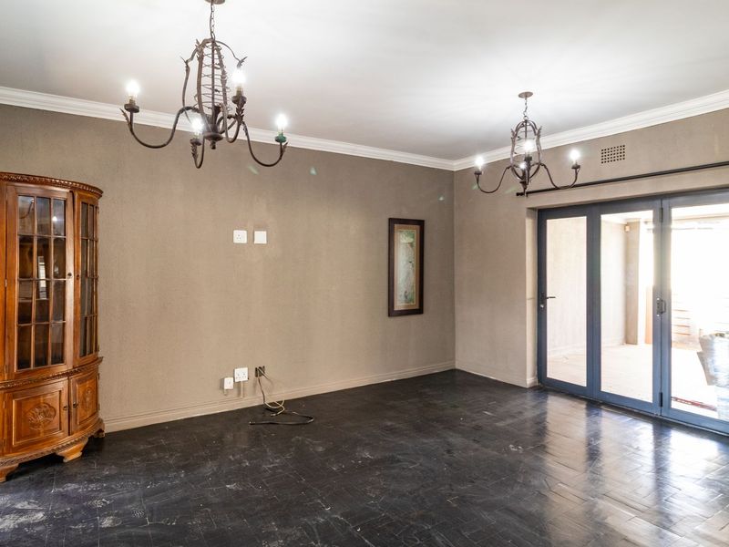Spacious living room featuring dark parquet flooring, crown molding, dual wrought iron chandeliers, and sliding glass doors providing access to the outdoor area.