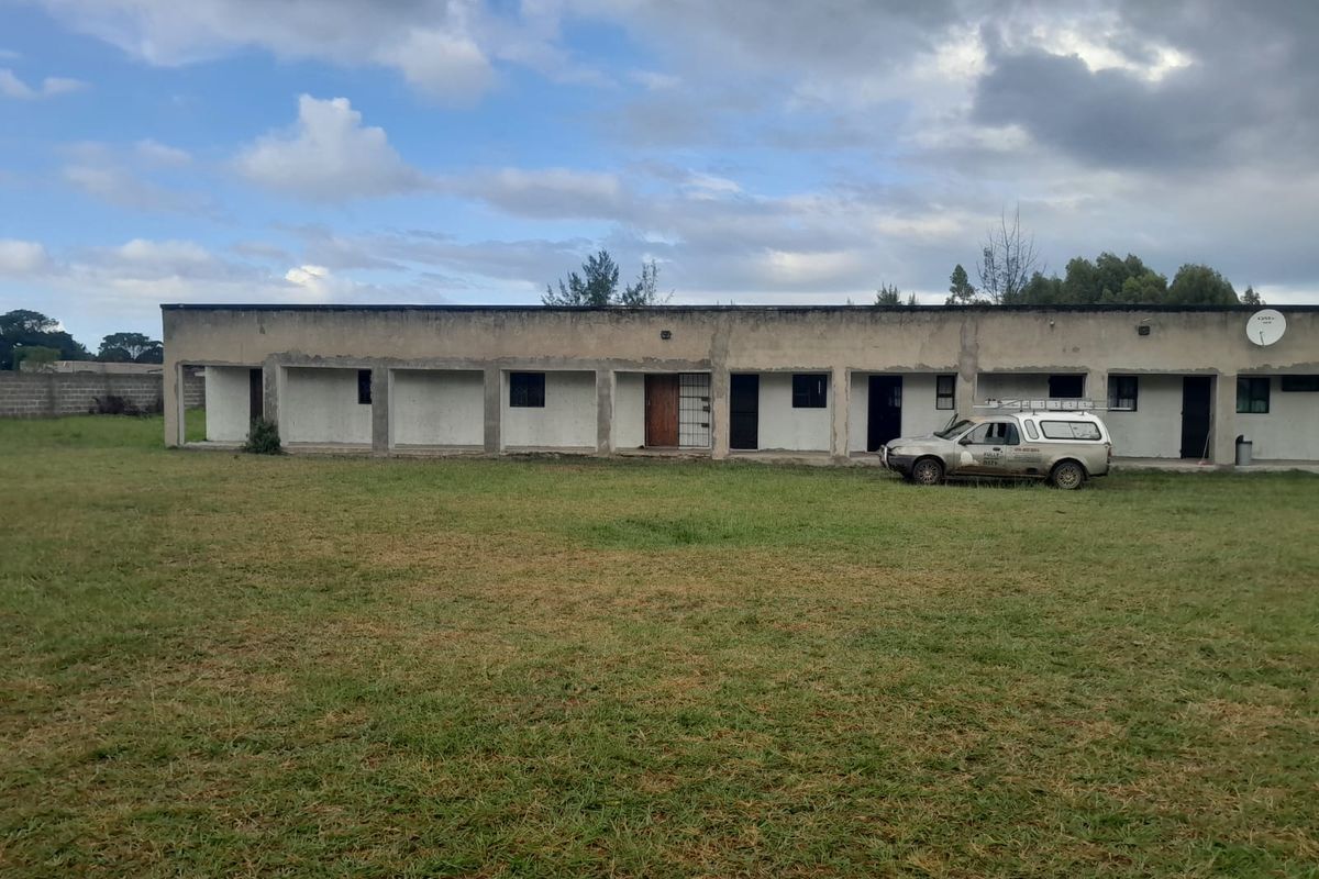 Rear view of a single-story cottage featuring a long covered veranda and a large open grass yard area.