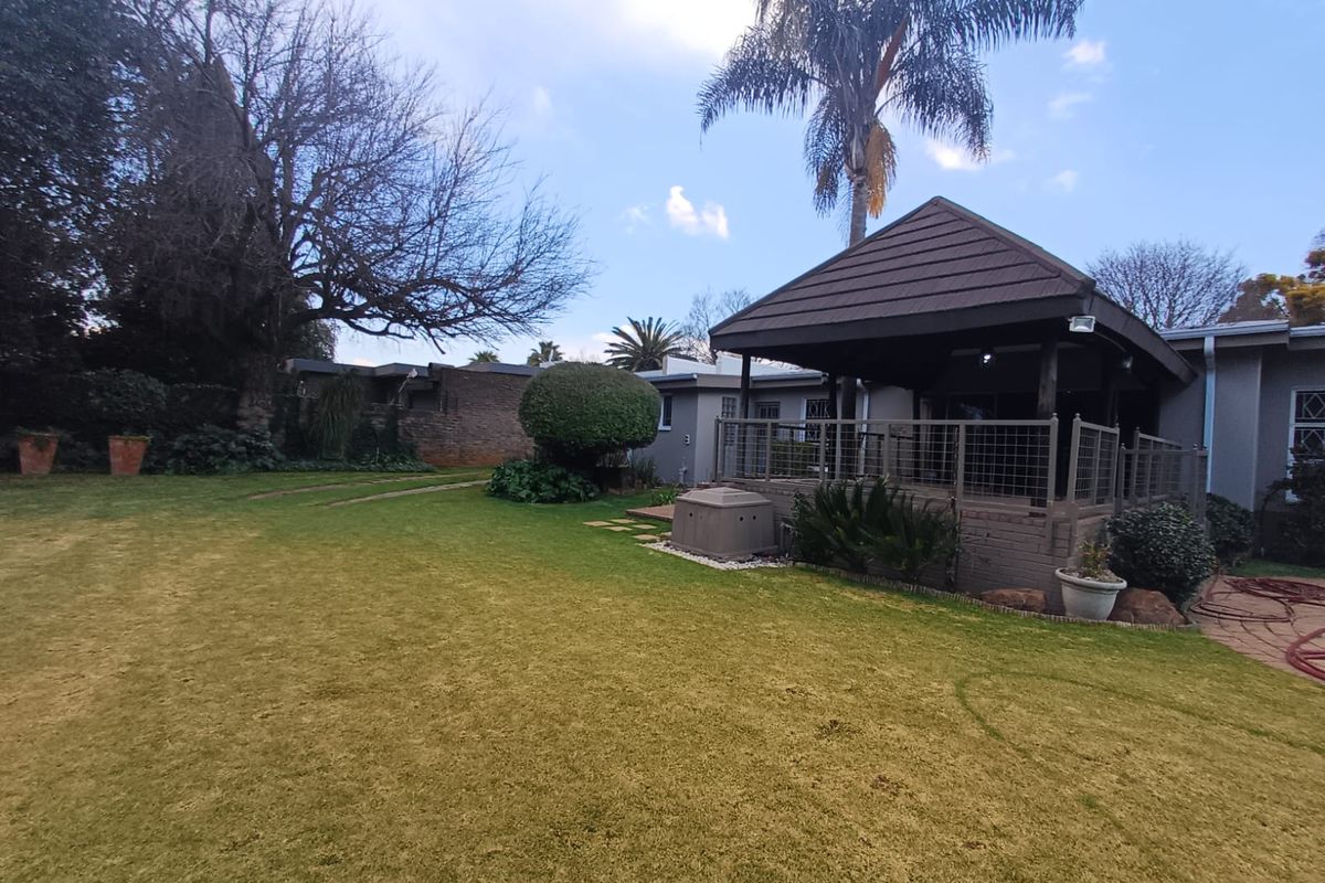 A spacious rear garden featuring a covered patio area with a tiled roof, well-maintained lawn, and established landscaping.