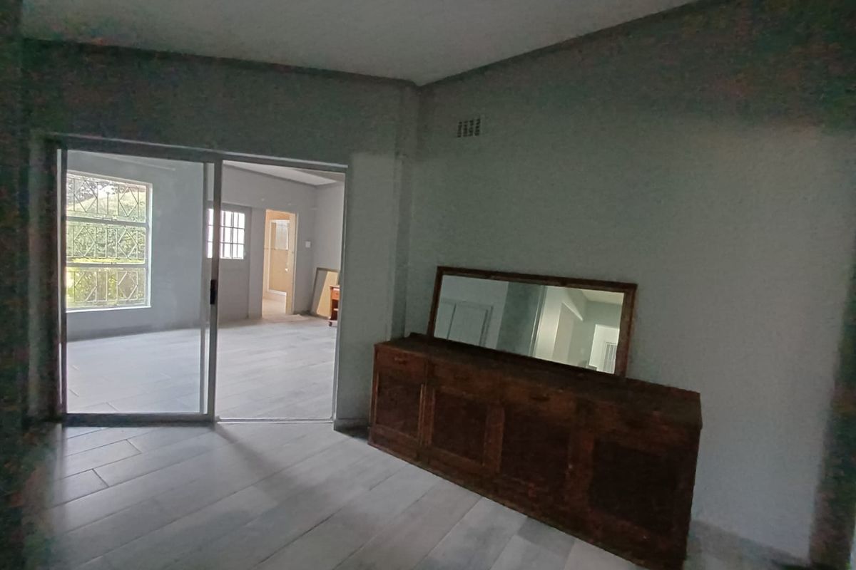 An open-plan living area featuring tiled flooring and a sliding glass door leading to an adjacent room, currently in need of finishing touches.