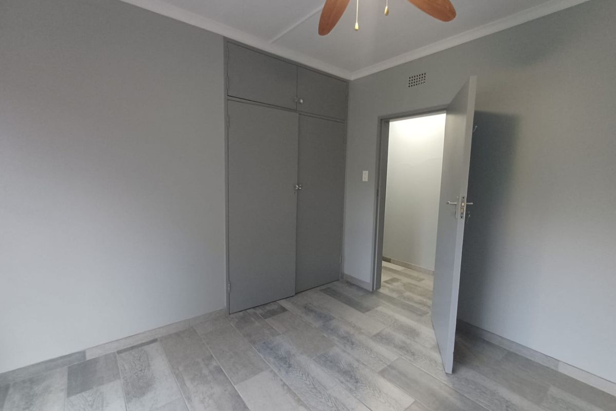 A clean, empty bedroom featuring modern grey tiled flooring, built-in cupboards, and a ceiling fan, offering a neutral canvas for personalization.