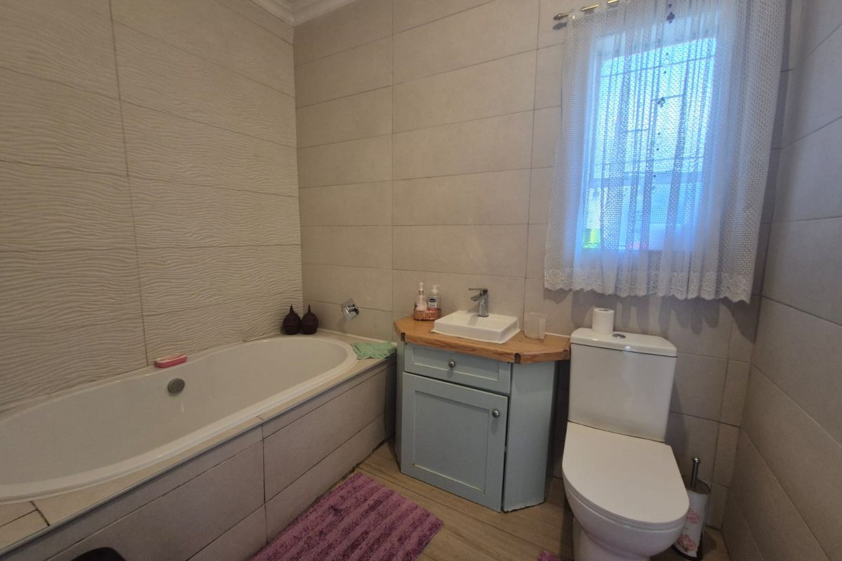 A functional bathroom featuring a built-in bathtub, a vanity cabinet with a basin, and a toilet, finished with neutral wall tiling.