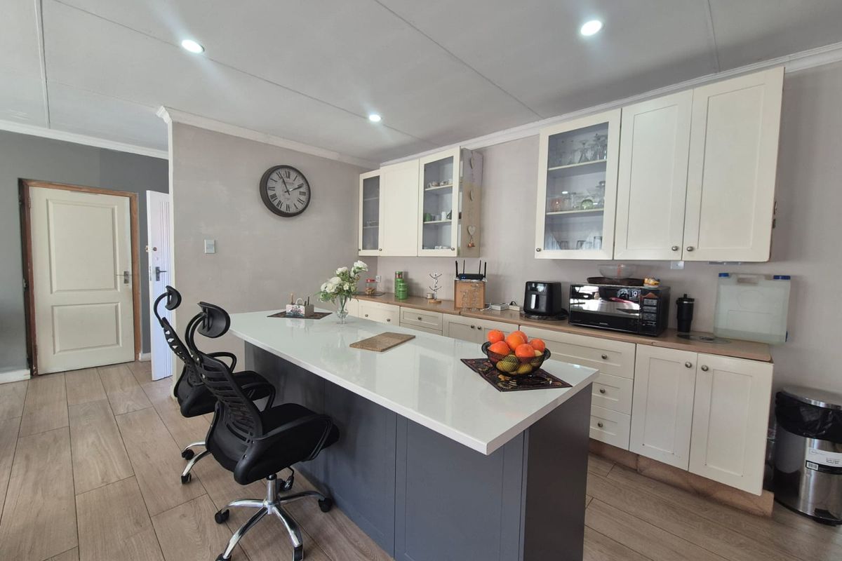 Modern kitchen featuring a central island with quartz countertops, shaker-style cabinetry, glass-front display units, and neutral tiled flooring.