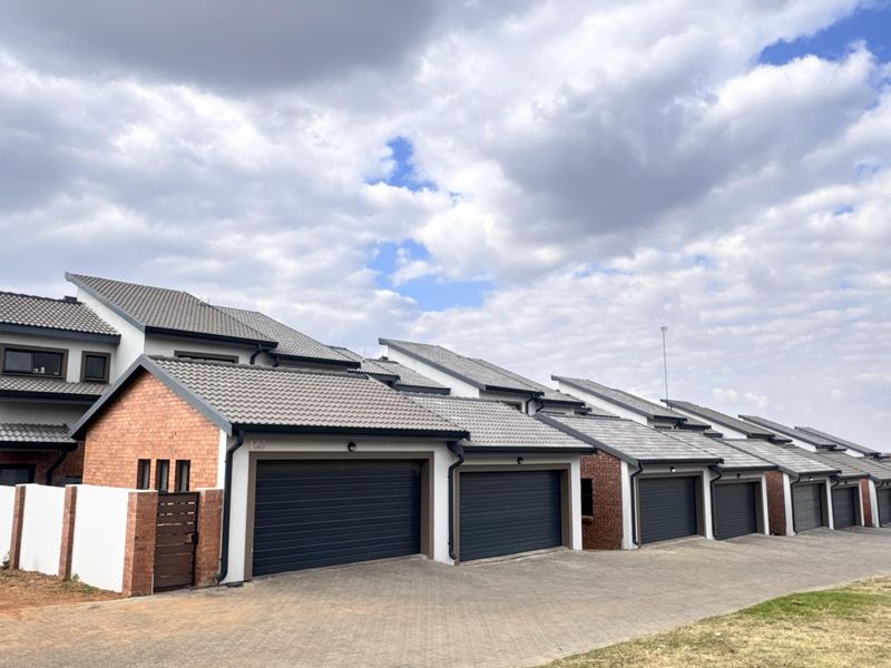 A row of modern townhouse units featuring brick facades, tiled roofs, and individual paved driveways with sectional garage doors.