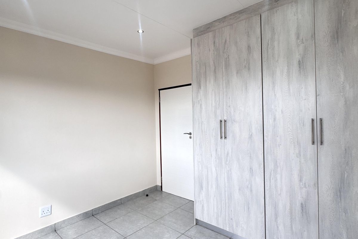 A clean, empty bedroom featuring modern grey wood-look built-in cupboards, neutral tiled flooring, and recessed ceiling downlights.