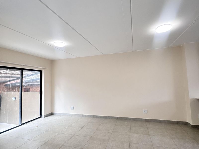 A bright, empty living area featuring neutral tiled flooring, recessed ceiling lighting, and a large sliding glass door providing access to the exterior.