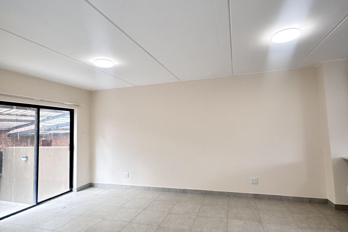 A bright, empty living area featuring neutral tiled flooring, recessed ceiling lighting, and a large sliding glass door providing access to the exterior.