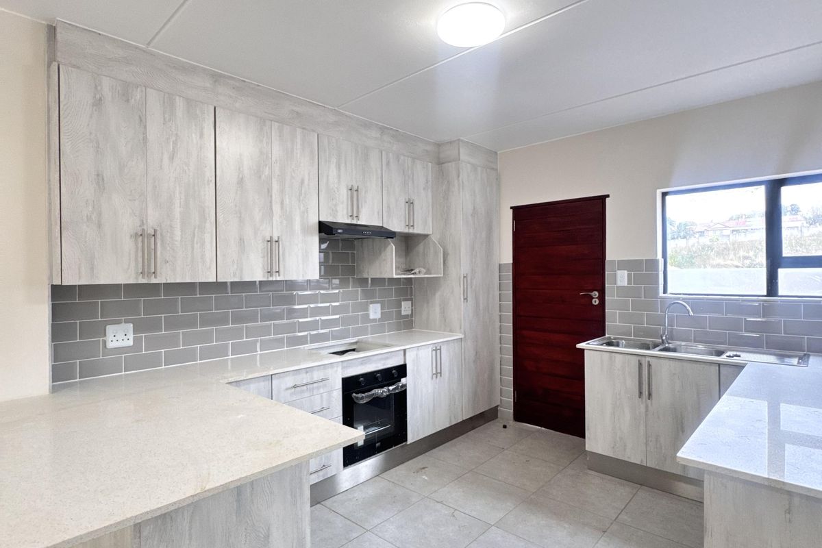 Modern kitchen featuring light wood-grain cabinetry, stone countertops, subway tile backsplash, built-in oven, extractor fan, and double bowl sink.