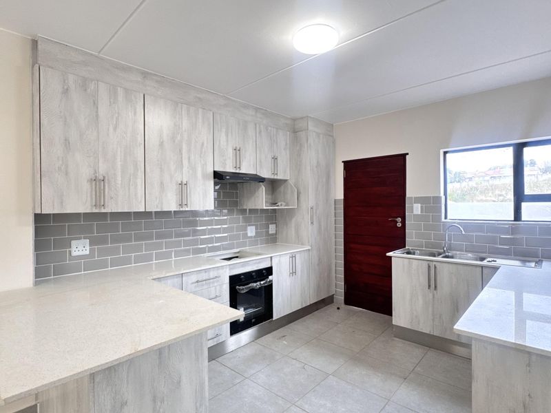 Modern kitchen featuring light wood-grain cabinetry, stone countertops, subway tile backsplash, built-in oven, extractor fan, and double bowl sink.