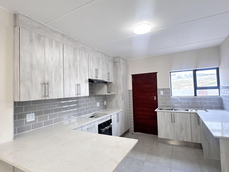 Modern kitchen featuring light wood-grain cabinetry, stone countertops, subway tile backsplash, and integrated appliances in a clean, open-plan layout.