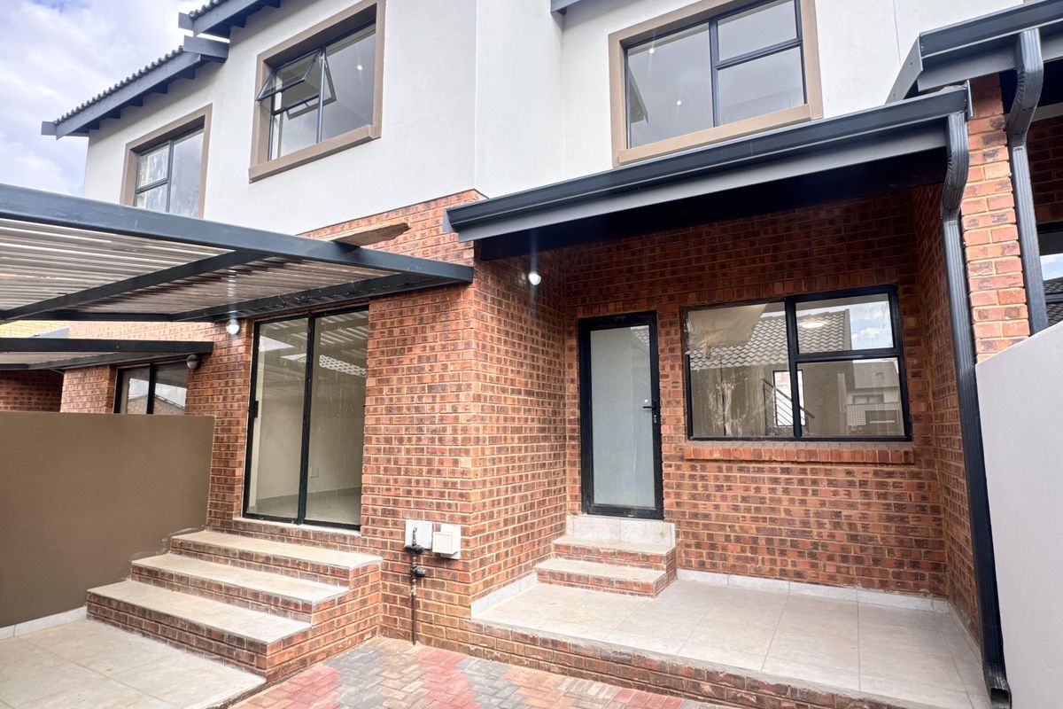 Rear view of a modern townhouse featuring a brick facade, paved courtyard, tiled patio area, and aluminum-framed windows and doors.