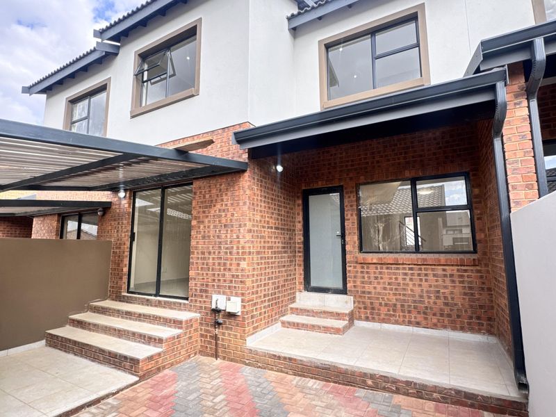 Rear view of a modern townhouse featuring a brick facade, paved courtyard, tiled patio area, and aluminum-framed windows and doors.