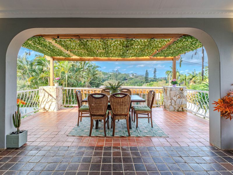 A spacious covered patio featuring terracotta tiling, stone-clad pillars, and a timber pergola, offering an elevated outdoor dining area with scenic views.
