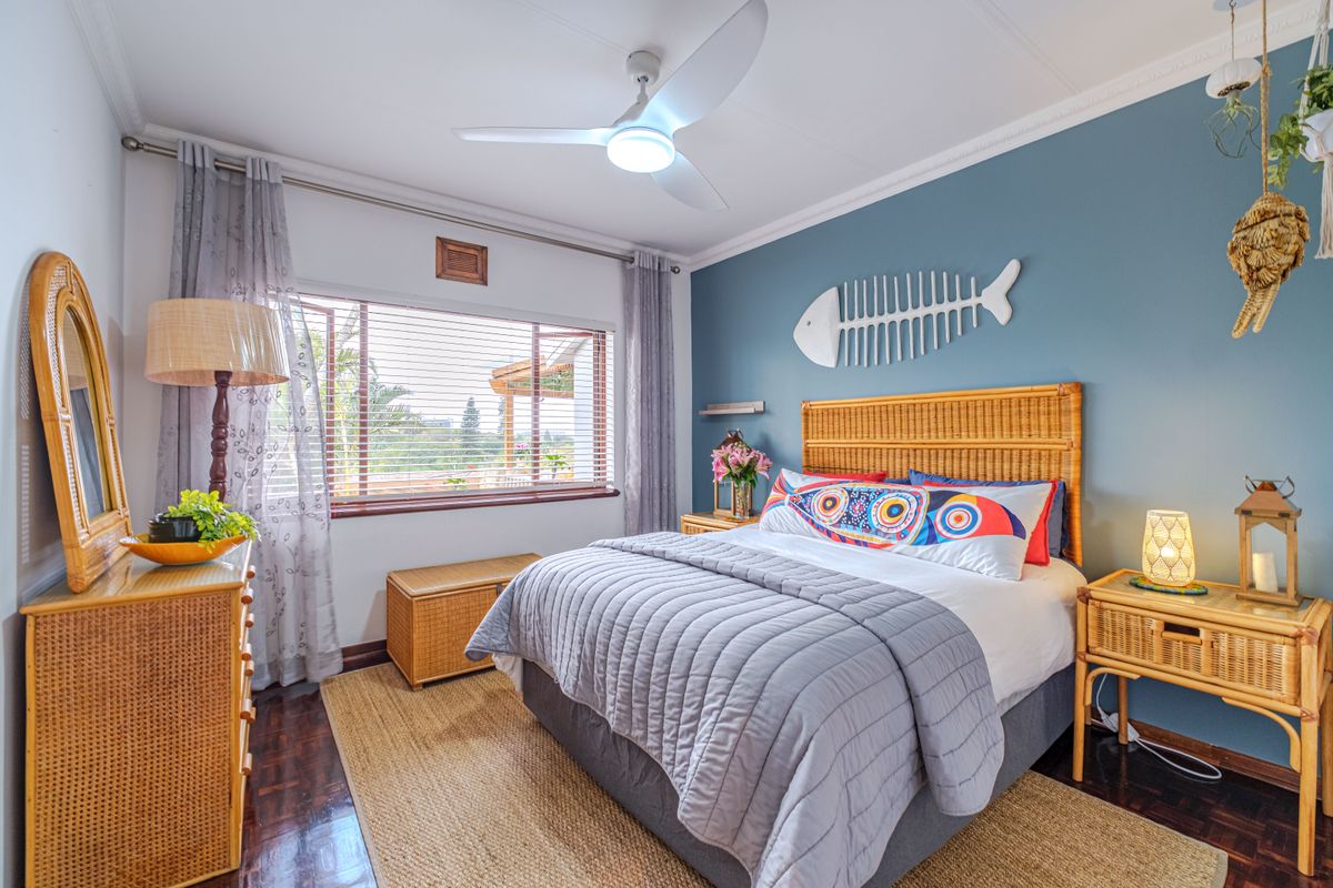A well-maintained bedroom featuring parquet flooring, a ceiling fan, and large windows with venetian blinds, creating a bright and comfortable living space.